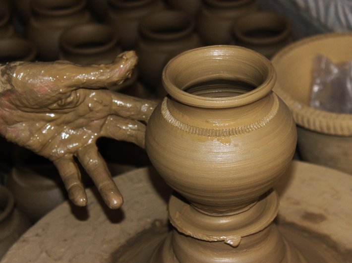 An earthen pot in making on a potter`s wheel